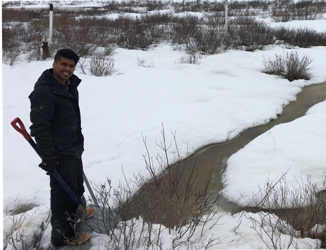 student Vaughn Mangal standing alongside a creed in snow with shovel in hand