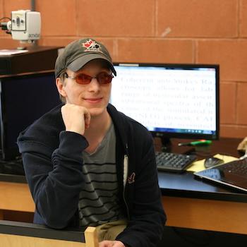 A student sitting in front of a computer with his chin resting on his hand and smiling
