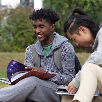 Students sitting on grass, laughing and looking at books