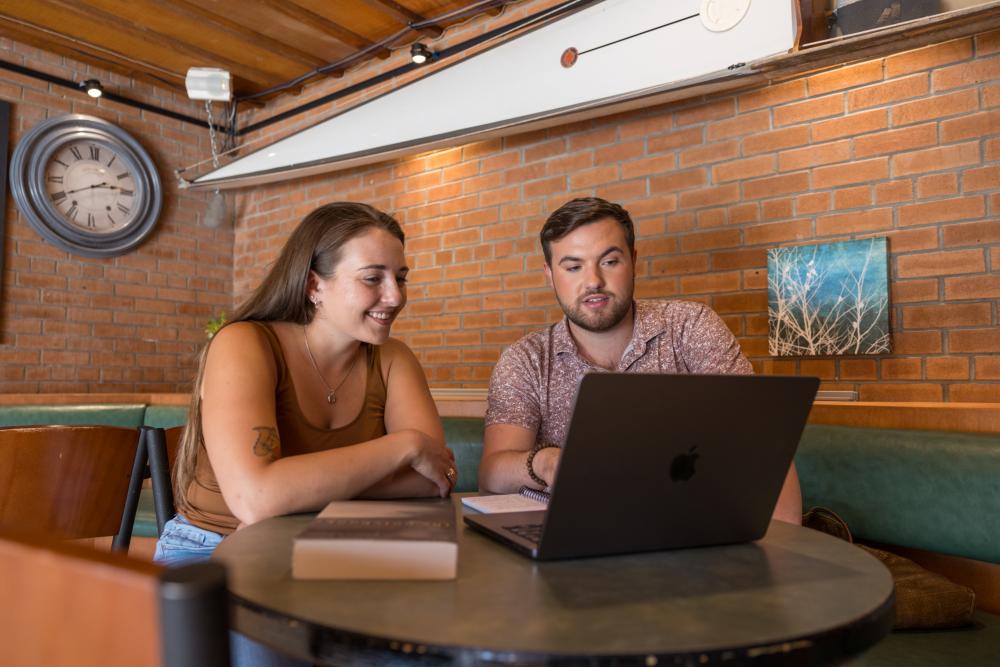 Two graduate students sit together at a table with a computer in front of them