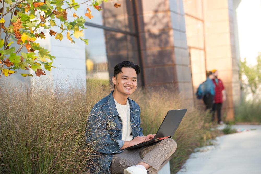 Student sitting outside of Trent Durham with laptop