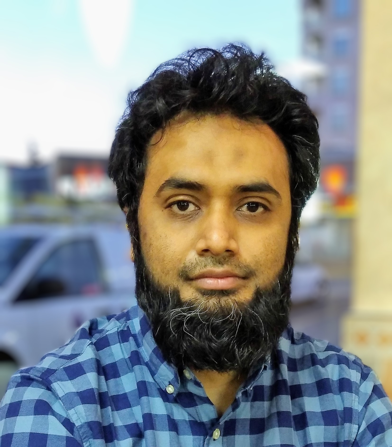 Image of a man with dark hair and a beard, wearing a blue checkered shirt.