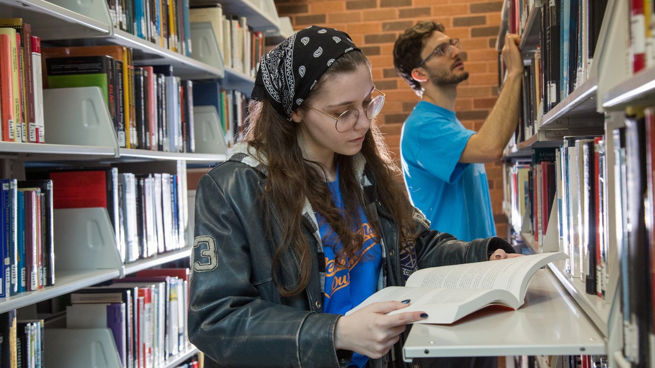 A student reading a book in the library stacks