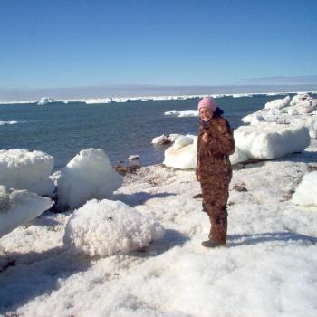 female standing on iceberg with winter camouflage clothing smiling at camera