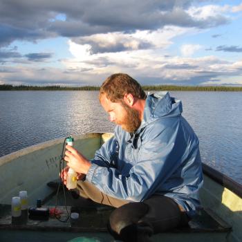 male sitting in boat on cloudy day wearing rain suit taking / analyzing water samples