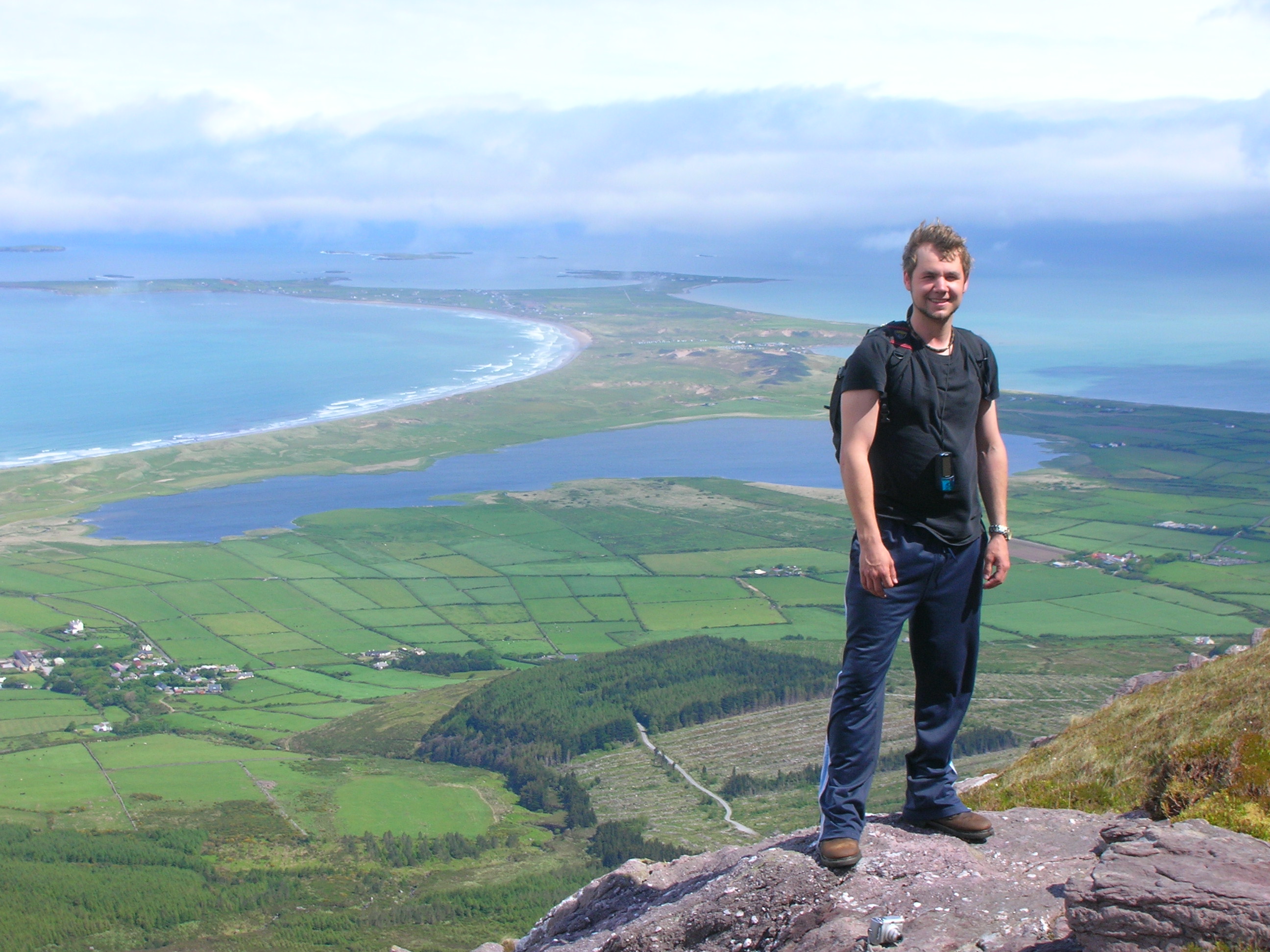 Andrew Burton, M.Sc graduate student standing at the top of a hill smiling at the camera