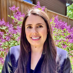 photo of Mary-Claire Buell, a smiling person with pale skin and light-brown long hair, wearing a blue shirt with flowers in the background