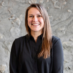 photo of Dr Buell, a smiling person with pale skin and light-brown long hair, wearing a black shirt against a grey background