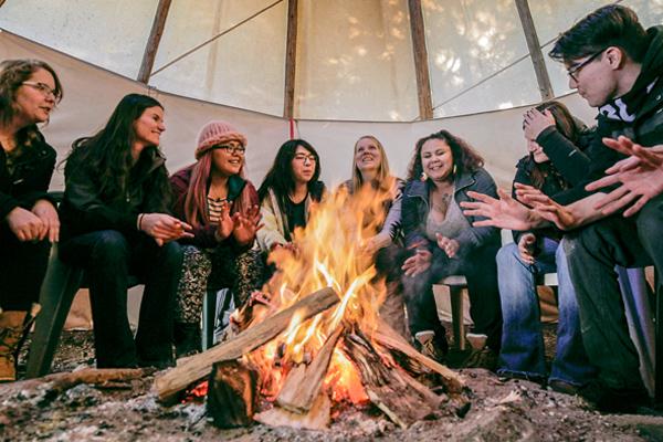 A group of students sitting around a bonfire inside a tipi