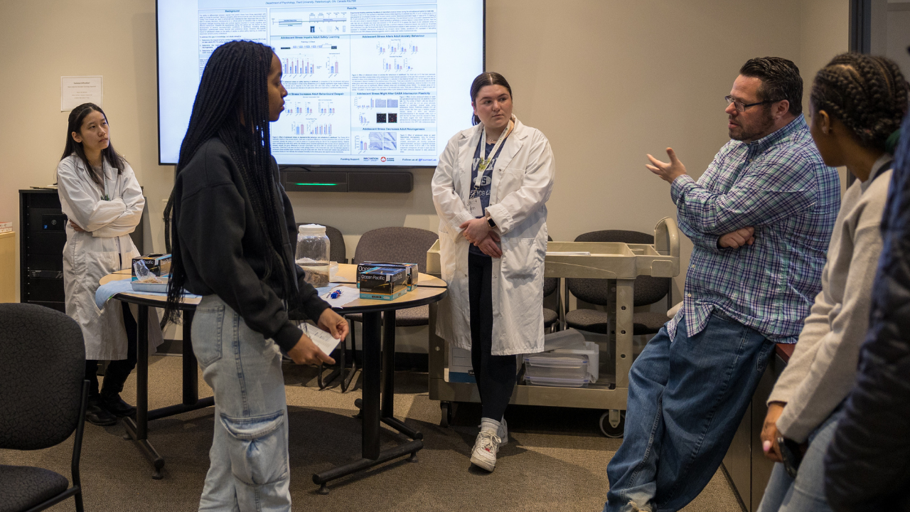 Professor and students in lab coats, talking to a student about the program.