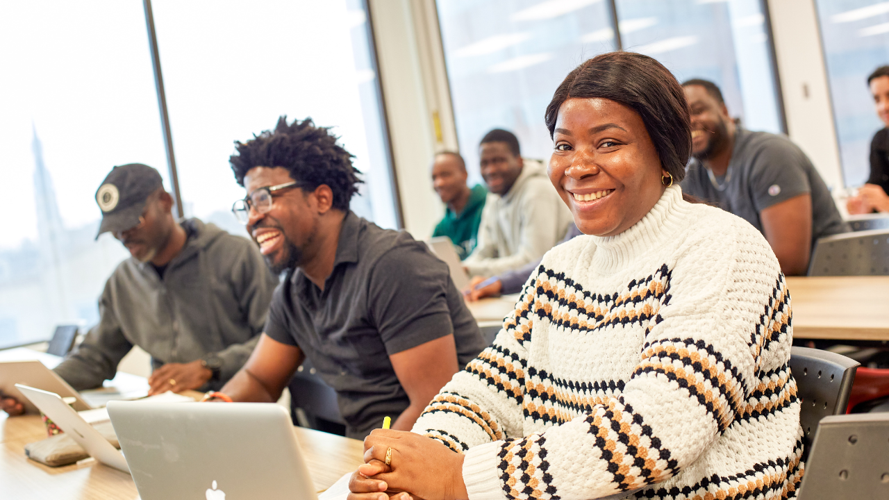 A postgraduate certificate lecture is happening in Trent Durham’s Advance Learning Centre, a student is smiling at the camera, with other students in the background listening to the professor.