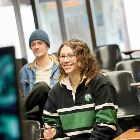 Trent University student in lecture, smiling towards the professor.