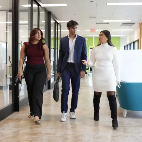 Three business students walking down an office hallway, talking to each other.