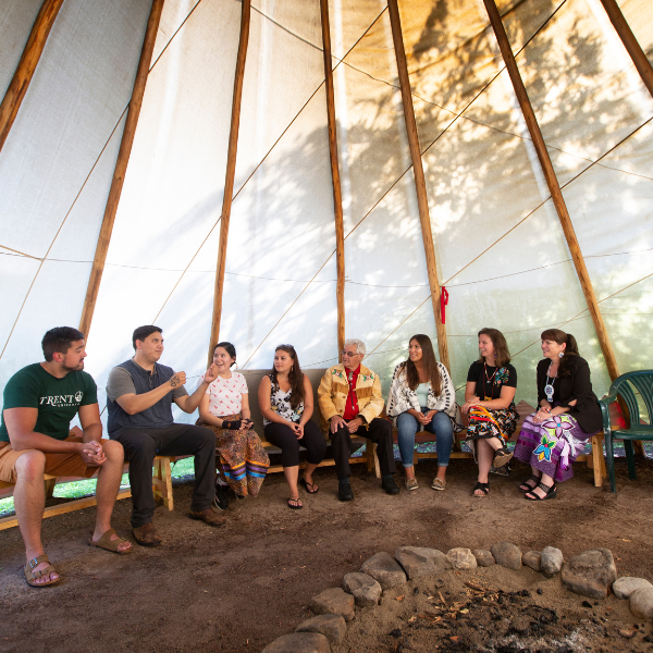 Group of Trent University First Peoples House of Learning staff and students talking inside of a tipi.  