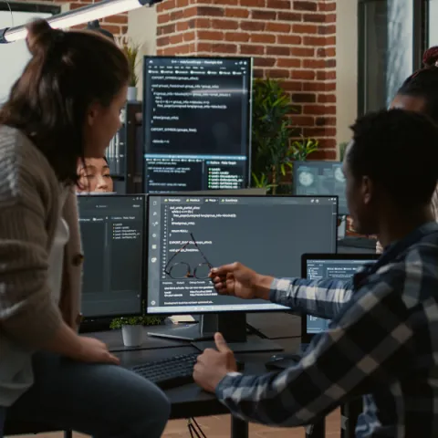 People sitting together, looking at a computer screen with code.