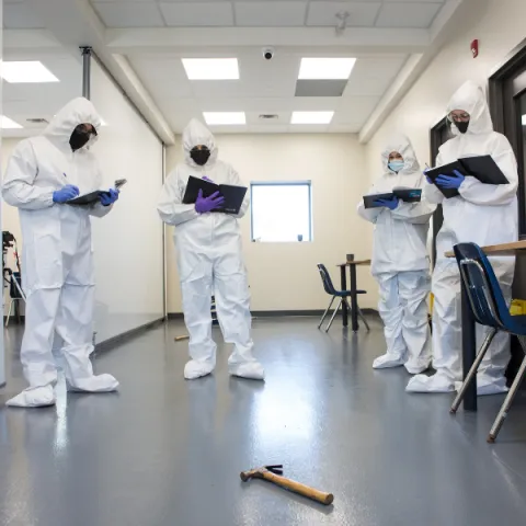 Trent University Forensics science students in lab, looking at hammer on the ground.