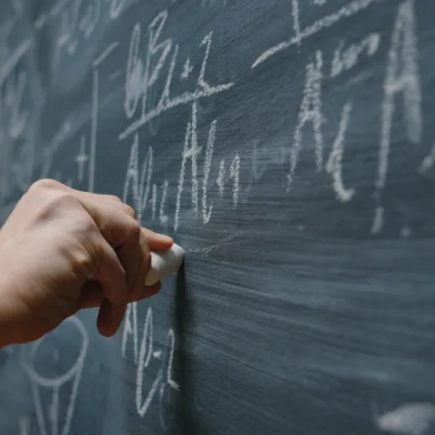 Mathematical physics equation being written on a chalk board.