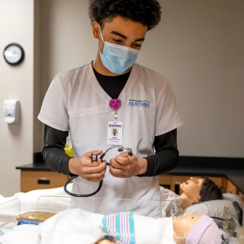 Trent University student in nursing lab, working on a mock baby doll.