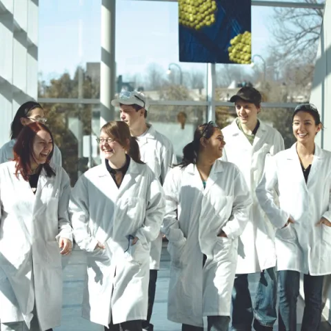 A group of Trent University science students, wearing lab coats, walking down the chemical science building hallway.