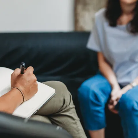 A therapist writing in a note book, while patience talks to them.