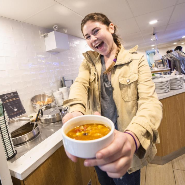 Student smiling and holding soup.