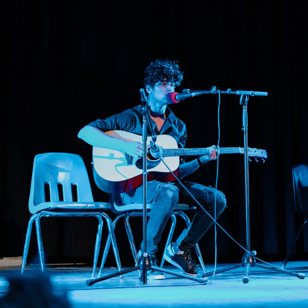 Student singing on stage with guitar.