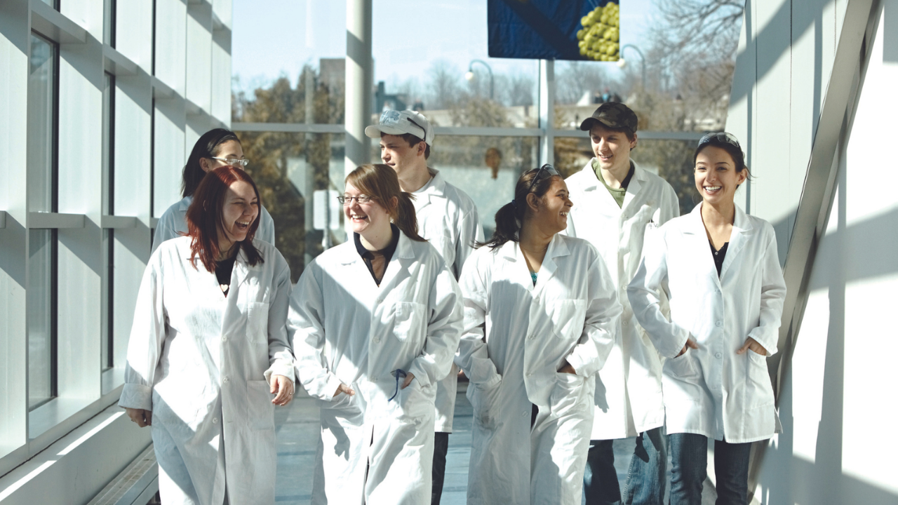 Group of students in hallway, wearing lab coats.