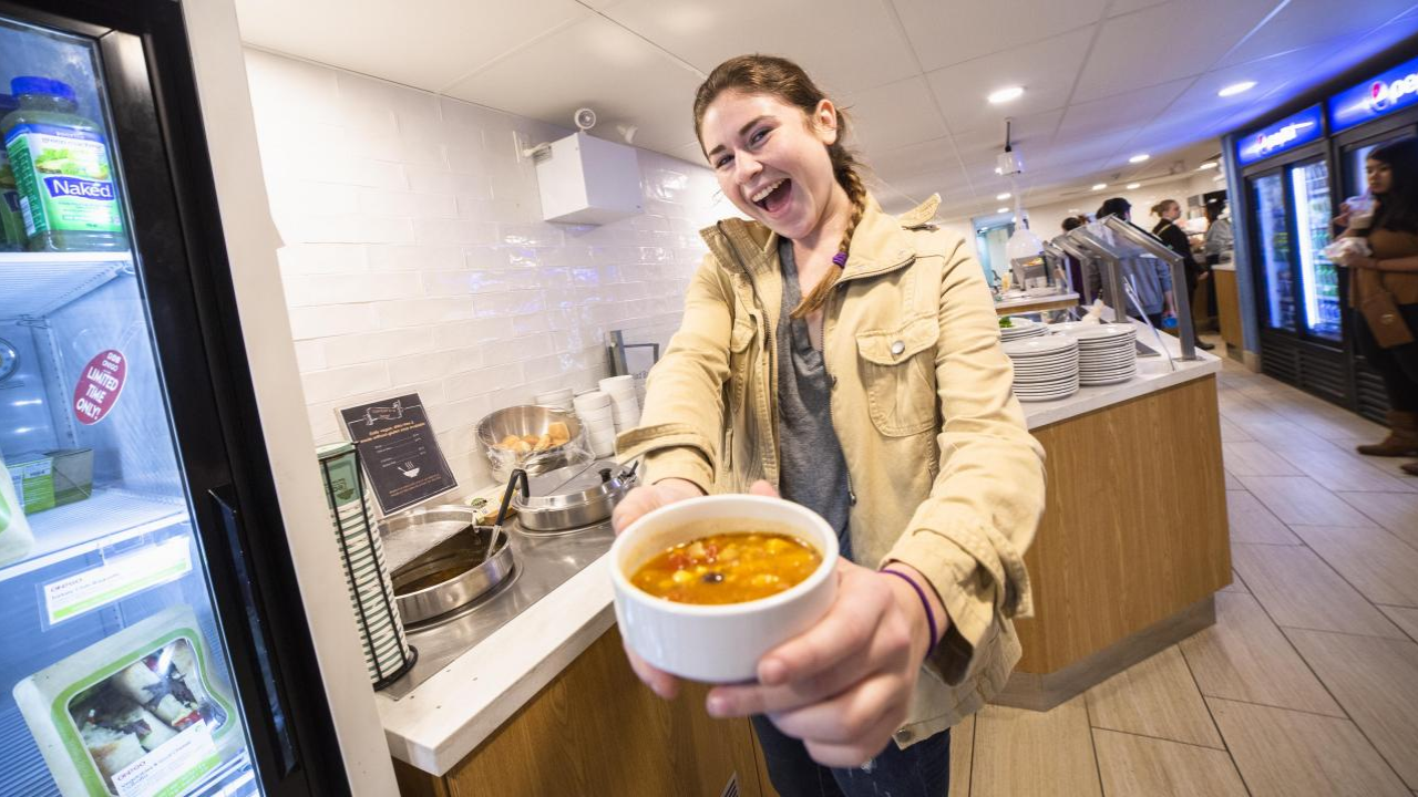 Student in dining hall holding soup.