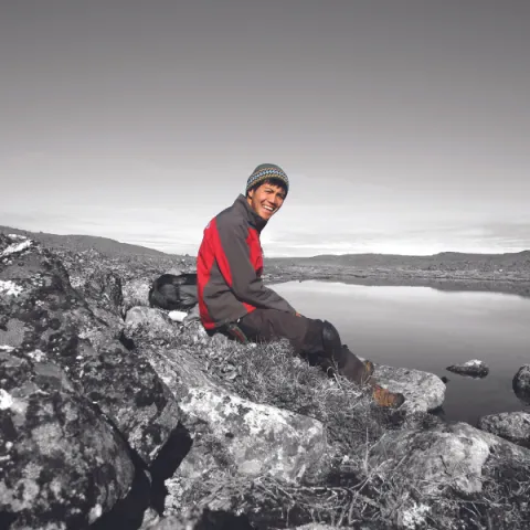 Student sitting on the top of a mountain, smiling at the camera.