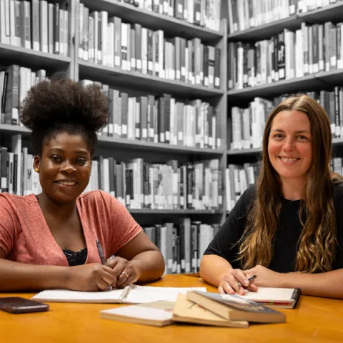 Two Trent University students smiling at the camera, with book shelves in the background.