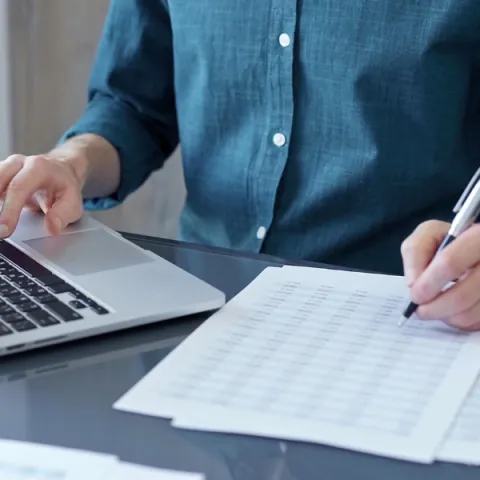 Business person is analyzing data on laptop and paper.