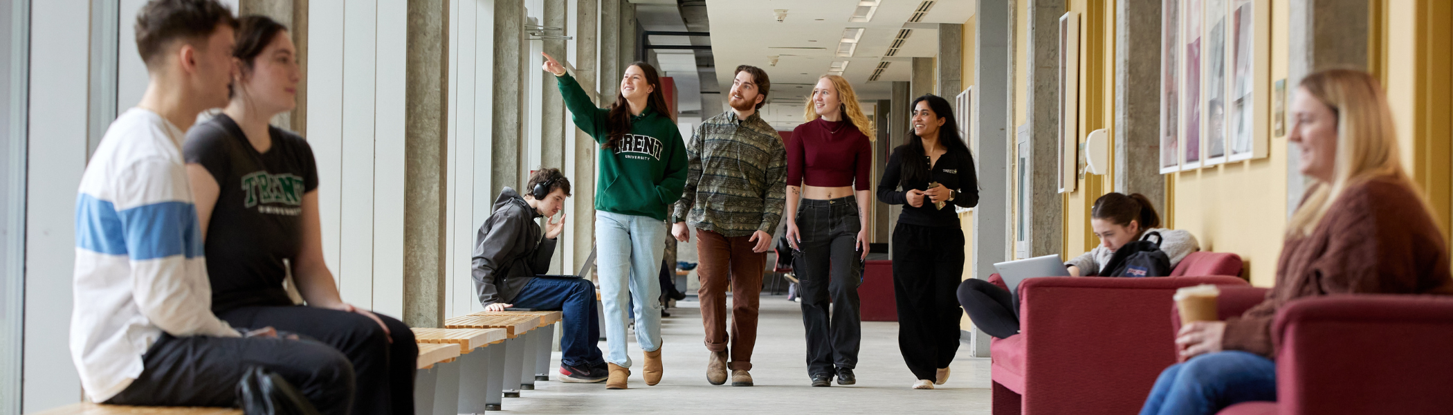 A group of Trent students walking down a hallway, one student is pointing outside.