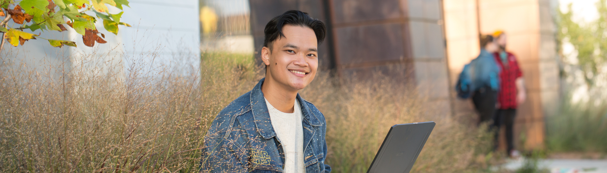 Student smiling at camera, on laptop.