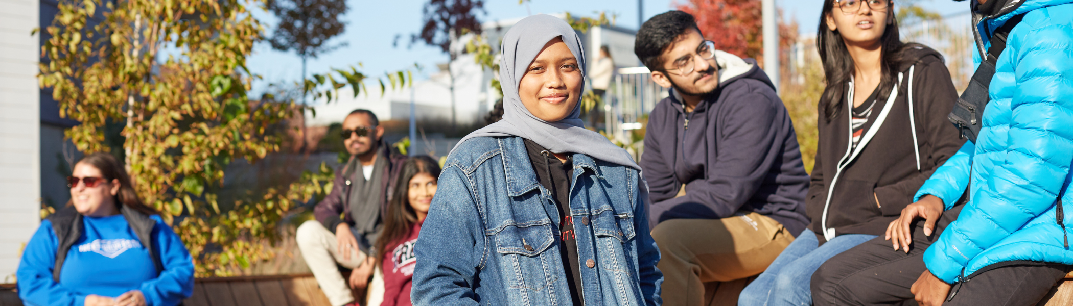 Trent Durham student smiling at camera, in front of a group of students talking outside. 