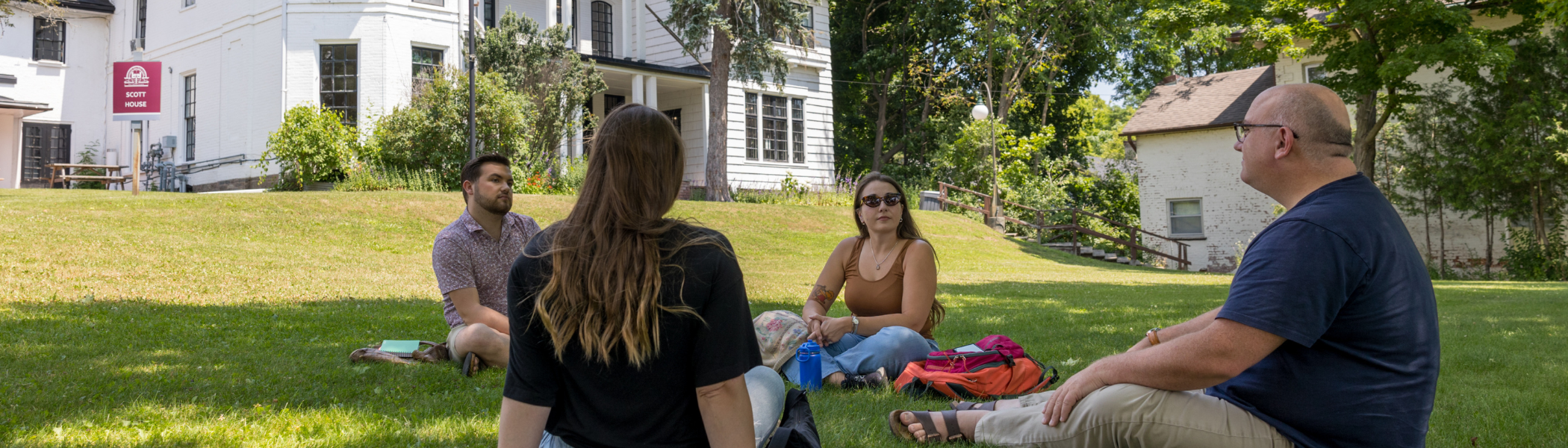 Four Trent Graduate studies students, sitting on Scott House front yard talking.