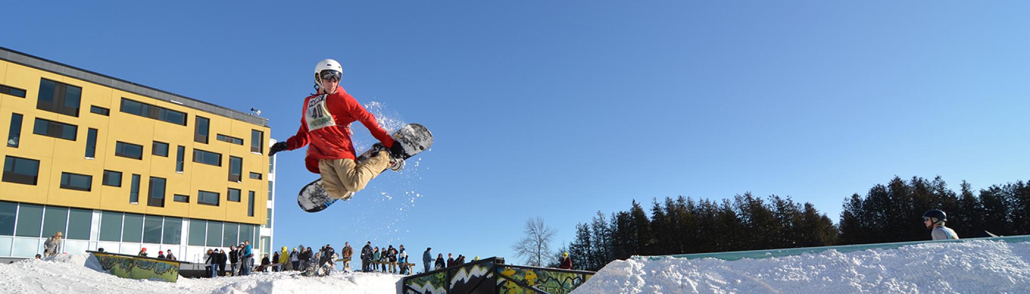 Student performing a snowboard air trick during railjam in the witer time