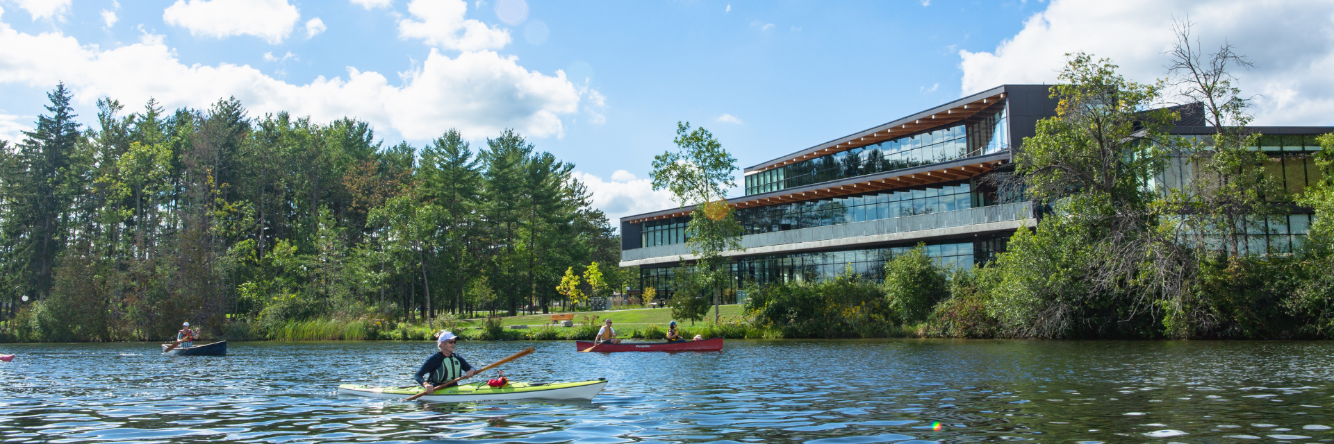 People in kayaks and canoes in the Otonabee river by the student centre