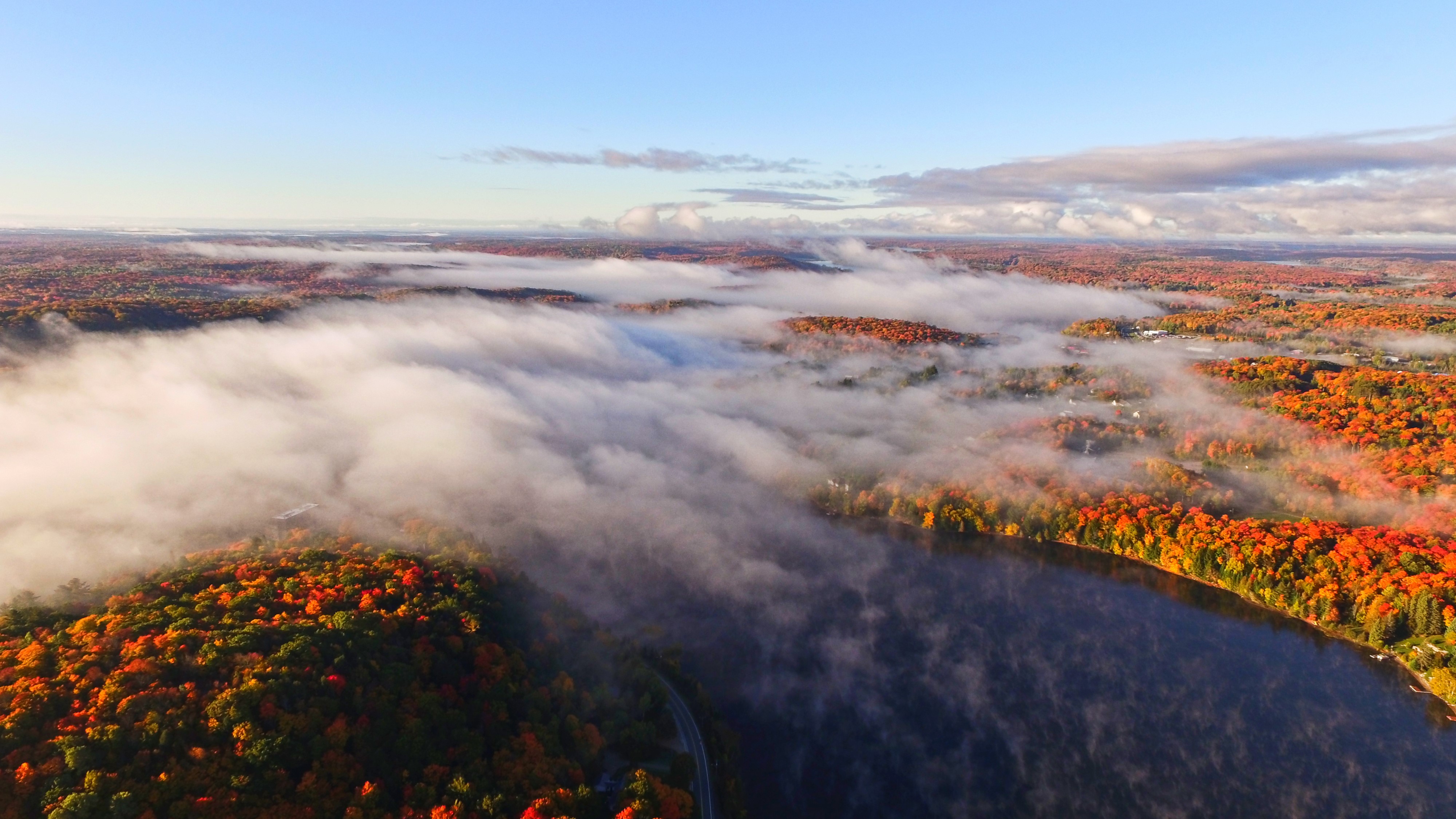 birds eye view of land with colourful fall trees, water and clouds above.