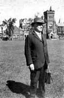 Black and white photograph of a man in a suit carrying a briefcase, standing on grass with a building in the background