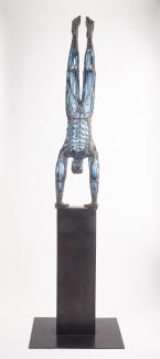 Glass blown figure of a person in a handstand. Sculpture is sitting on a black platform. 