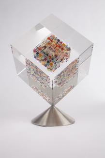Glass sculpture in shape of cube that is clear around edges and multicoloured in the center.