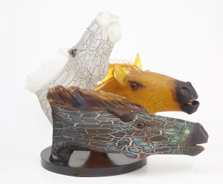 Three horse heads made of glass. One horse is white, another is yellow and the third is brown with shades of green. 