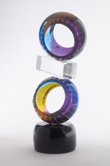 Glass sculpture in shape of figure 8 with two multicoloured glass circles separated by clear rectangular piece of glass