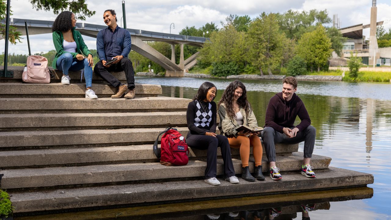 Students sitting on the bank of the Otonabee River